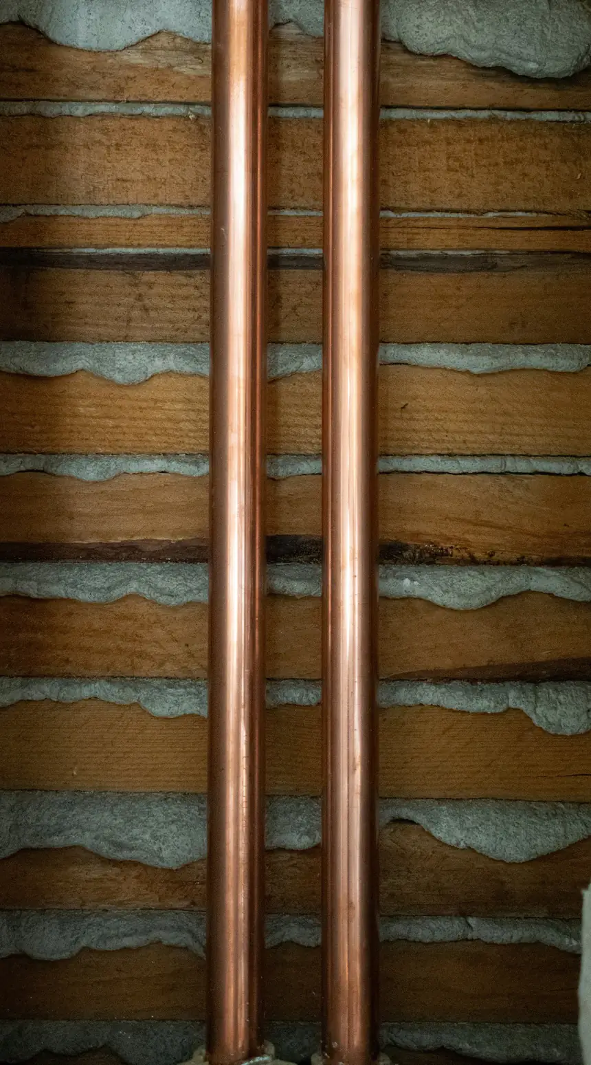 Photo d’illustration : deux tubes de cuivre posés verticalement dans une cloison ouverte.